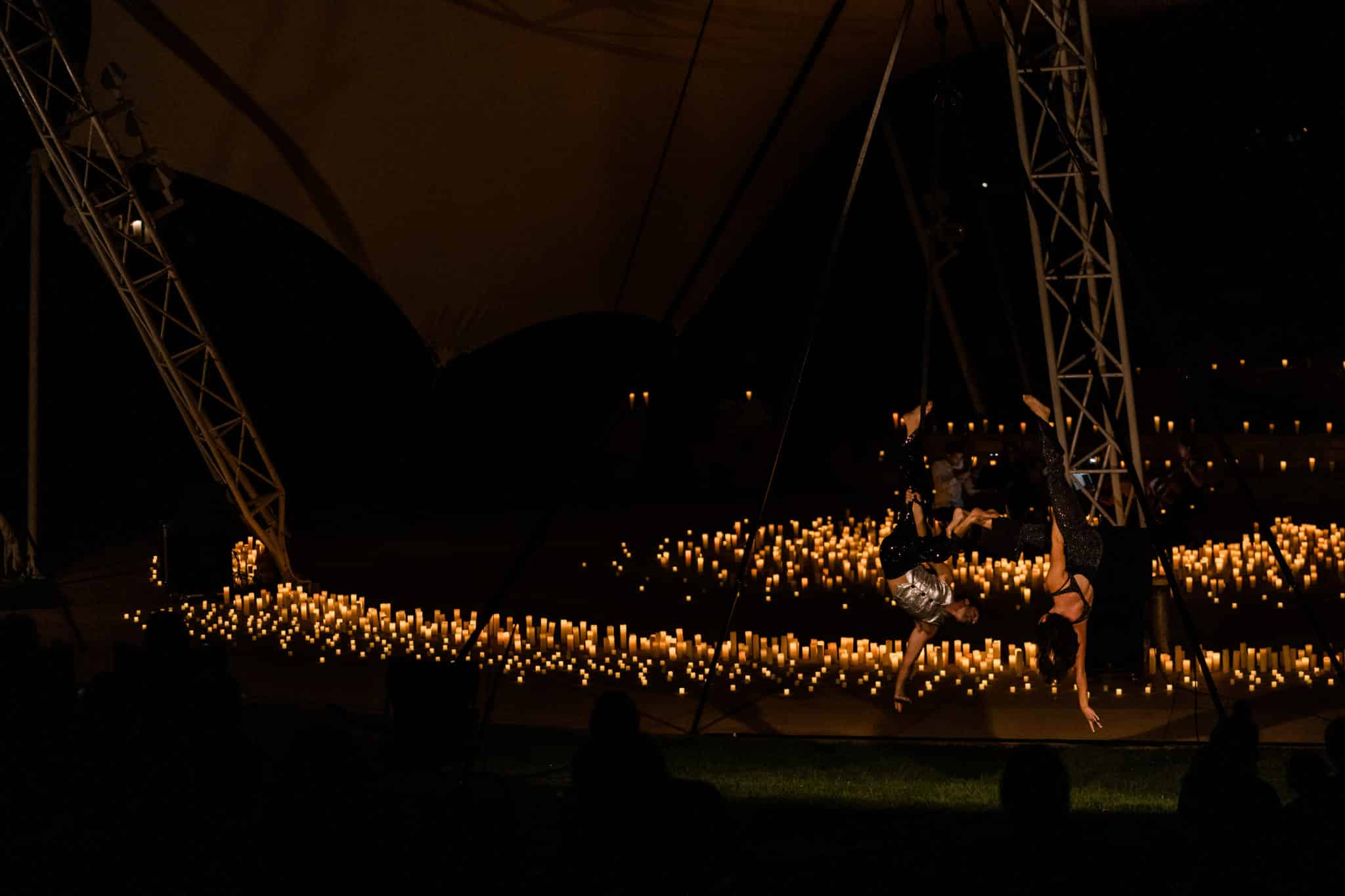 Aerialists performing on one side of a stage covered in candles at an open-air Candlelight concert in Denver.