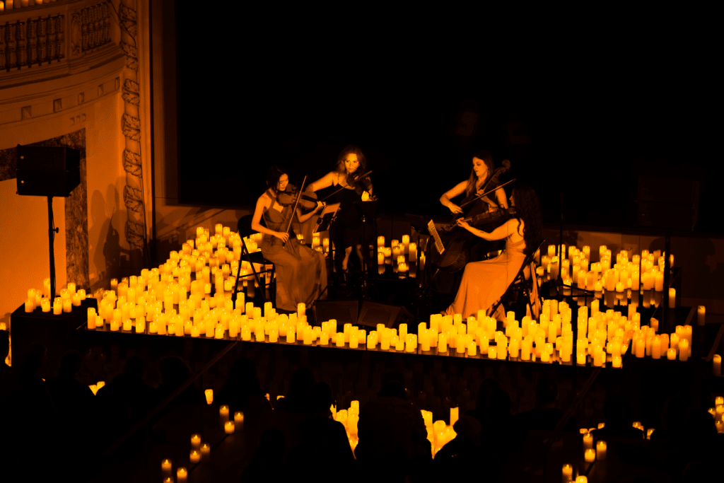A string quartet performing on a stage surrounded by candles.