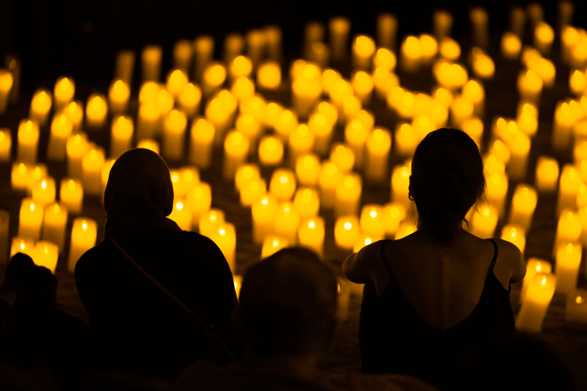 The silhouette of three people looking out across a sea of candles.