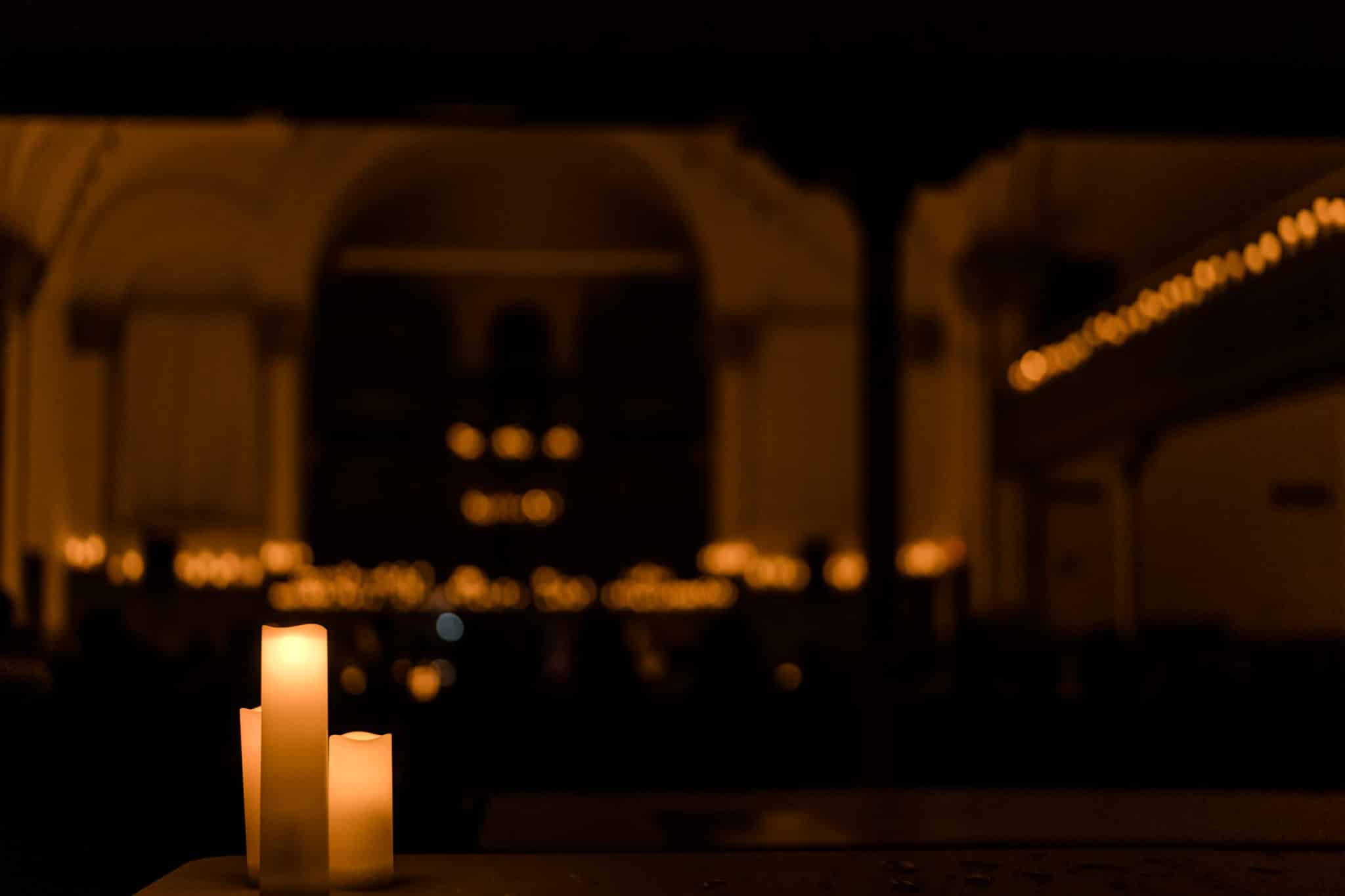 A close-up of three candles with a blurred background of a candlelit performance.