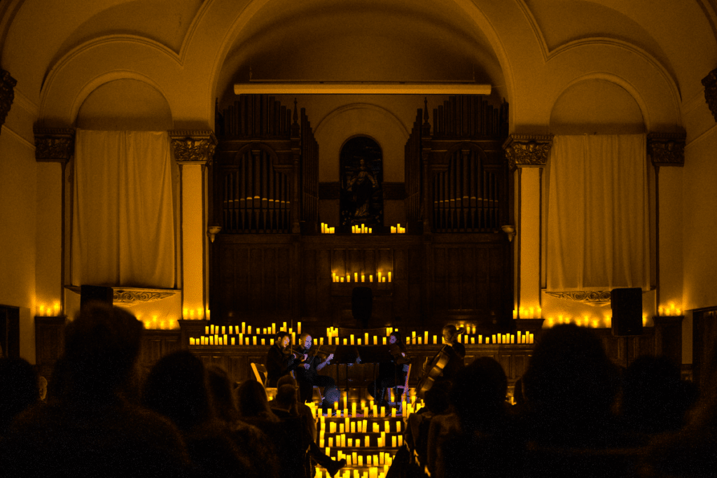 Inside of a church space with a stage convered in candles and a string quartet performing.