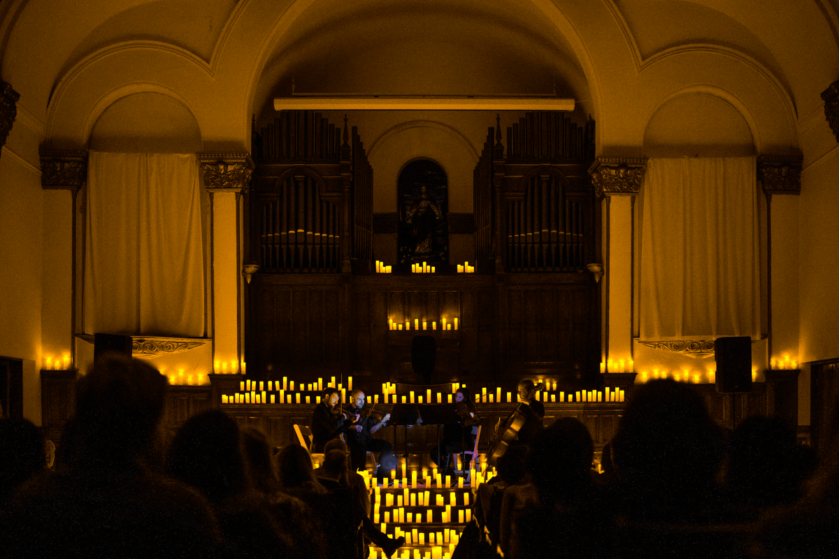 Inside of a church space with a stage convered in candles and a string quartet performing.