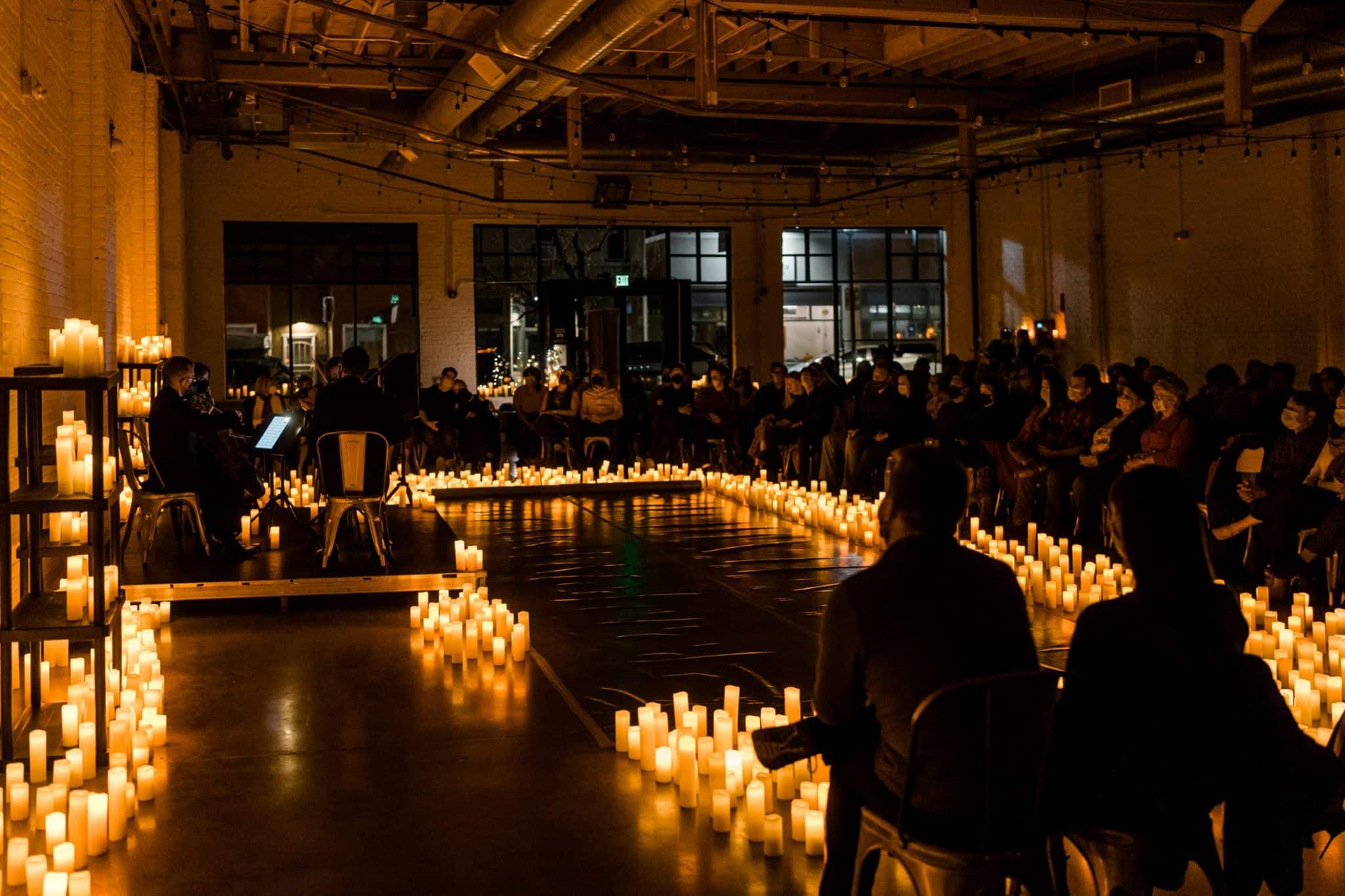 An audience is sitting around a stage lined by candles while a string quartet is performing. 