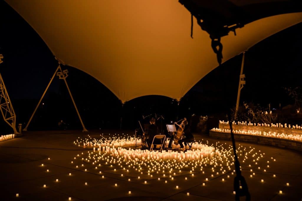 A string quartet is performing underneath a canopy on a stage covered in candles.