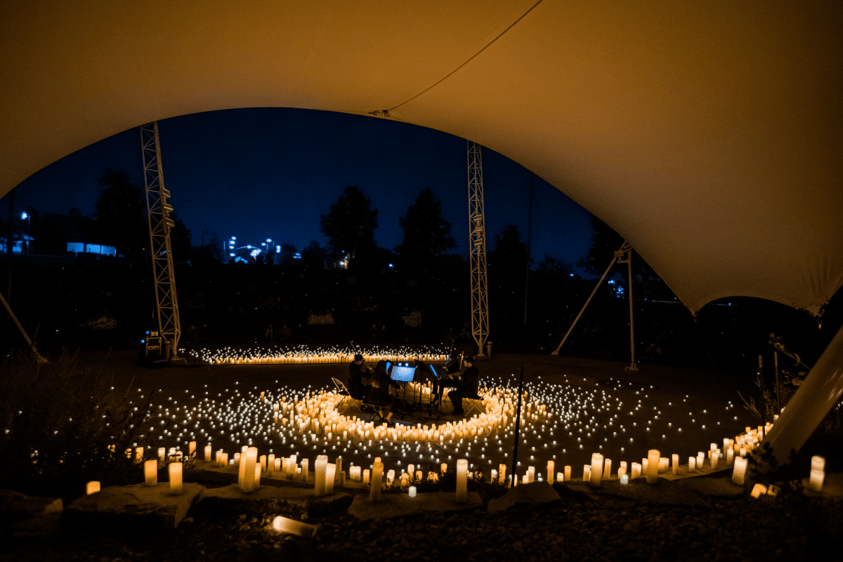 An open-air Candlelight concert taking place underneath a huge canopy with a string quartet performing on stage surrounded by hundreds of candles.