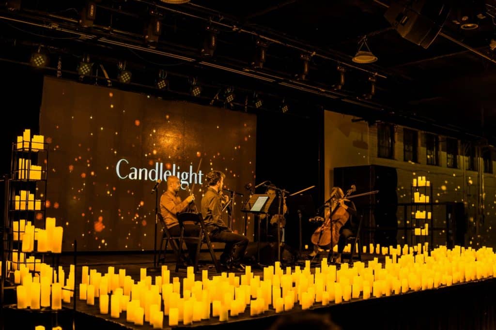 A string quartet performing on stage while surrounded by hundreds of candles